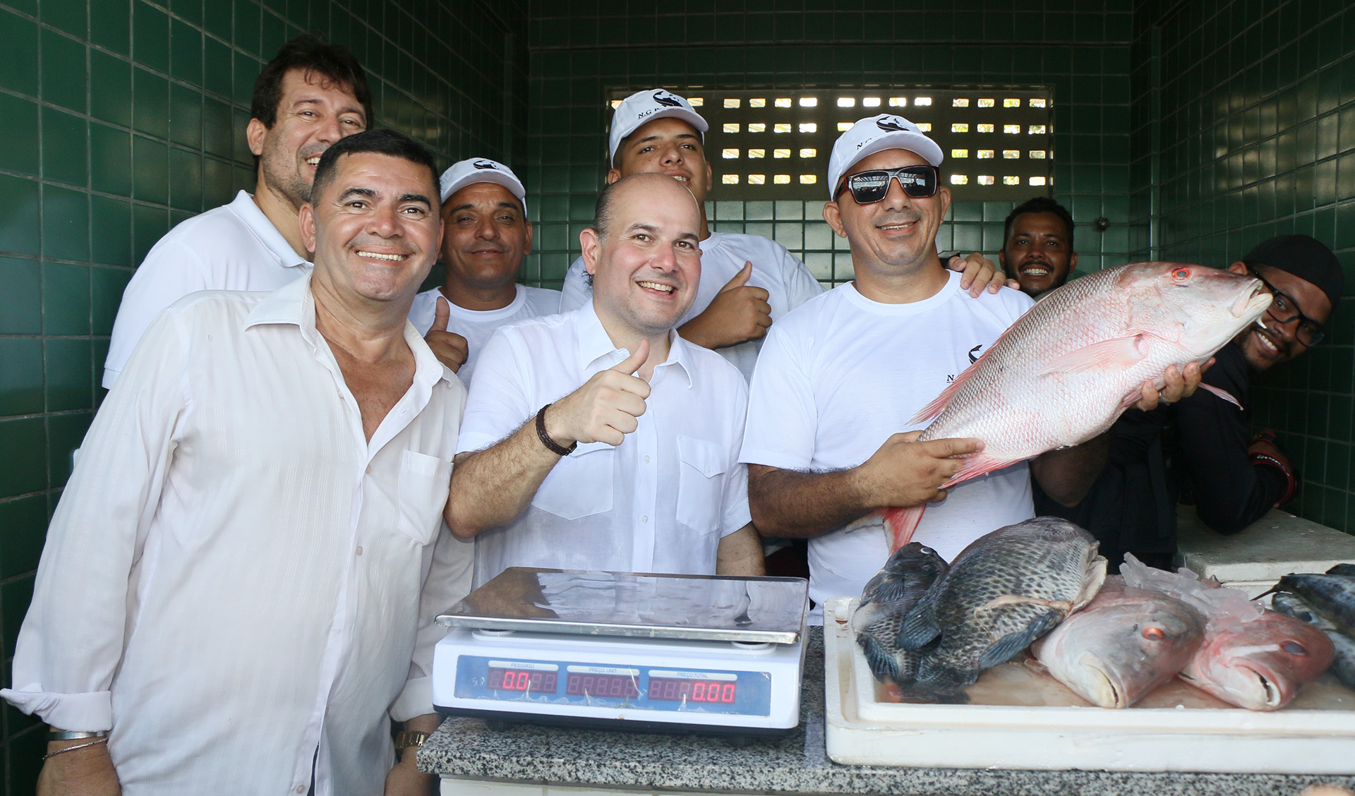 prefeito ao lado de homens e vendedor segurando peixe
